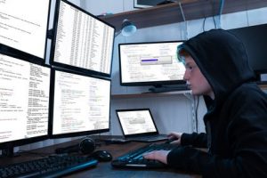 Boy Programming On Computer With Multiple Monitors And Laptop On Desk